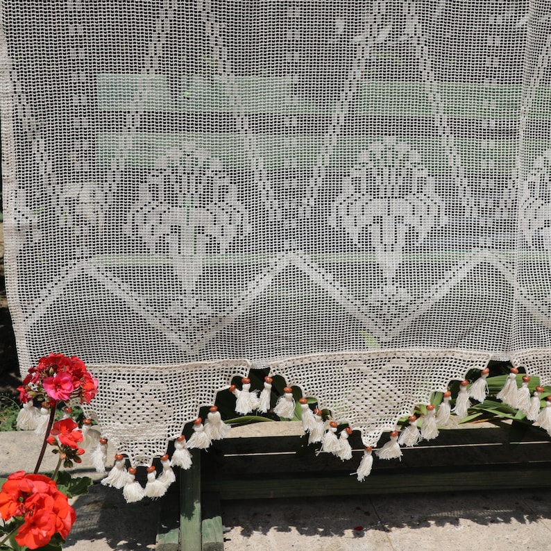 May include: White crocheted curtain with a delicate pattern and tassels along the bottom edge.