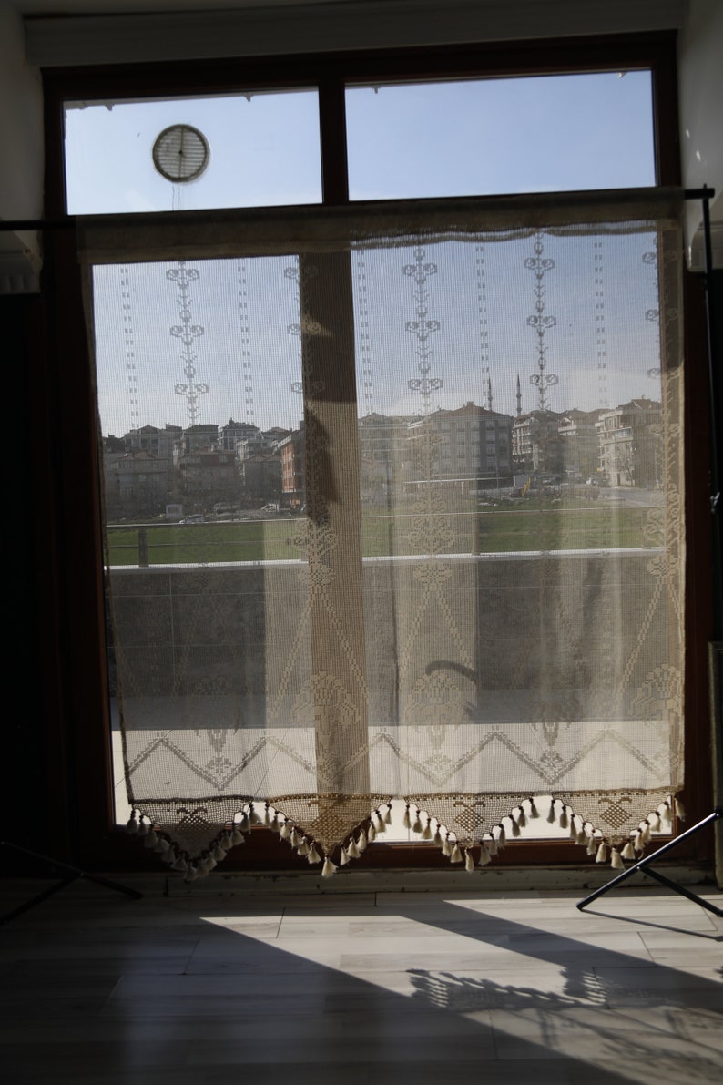 May include: A window with a sheer lace curtain, showing a view of a city skyline with buildings and a mosque in the distance.