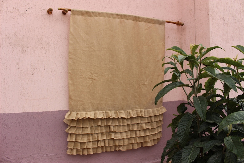 May include: A beige linen curtain with a ruffled bottom edge. The curtain is hanging on a wall with a pink and purple paint scheme.