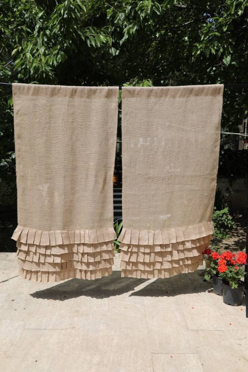 May include: Two brown burlap curtains with a ruffled bottom edge. The curtains are hanging on a clothesline.