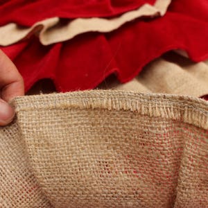 May include: Close-up of a brown burlap fabric with a frayed edge. The fabric is woven with a loose, open weave. The fabric is folded over itself, revealing a red fabric underneath.