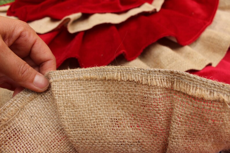 May include: Close-up of a brown burlap fabric with a frayed edge. The fabric is woven with a loose, open weave. The fabric is folded over itself, revealing a red fabric underneath.