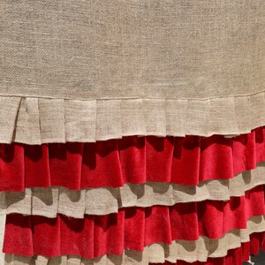 May include: A brown burlap fabric with a red velvet ruffle trim. The fabric has a woven texture and the ruffle is layered.