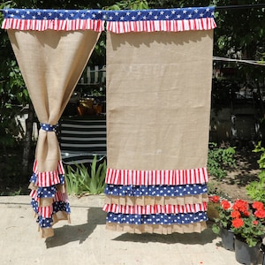 May include: Two burlap curtains with red, white, and blue ruffled trim. The trim features stars and stripes. The curtains are hanging from a rod.