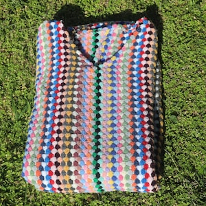 May include: A crochet top featuring a vibrant, multi-coloured pattern of small, raised circular stitches arranged in vertical stripes. The garment displays a wide spectrum of colours including red, blue, yellow, green, and orange, with a V-neckline.