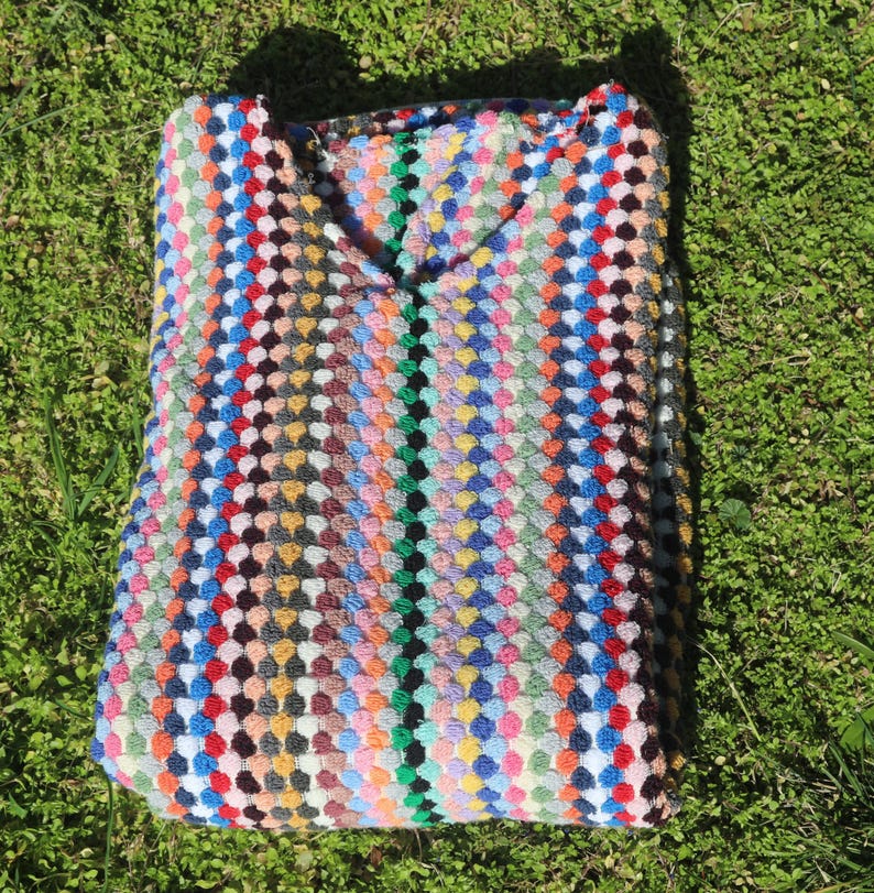 May include: A crochet top featuring a vibrant, multi-coloured pattern of small, raised circular stitches arranged in vertical stripes. The garment displays a wide spectrum of colours including red, blue, yellow, green, and orange, with a V-neckline.