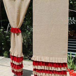 May include: Two burlap curtains with red velvet ruffles at the bottom. The curtains are hanging from a rod and are in a backyard setting.