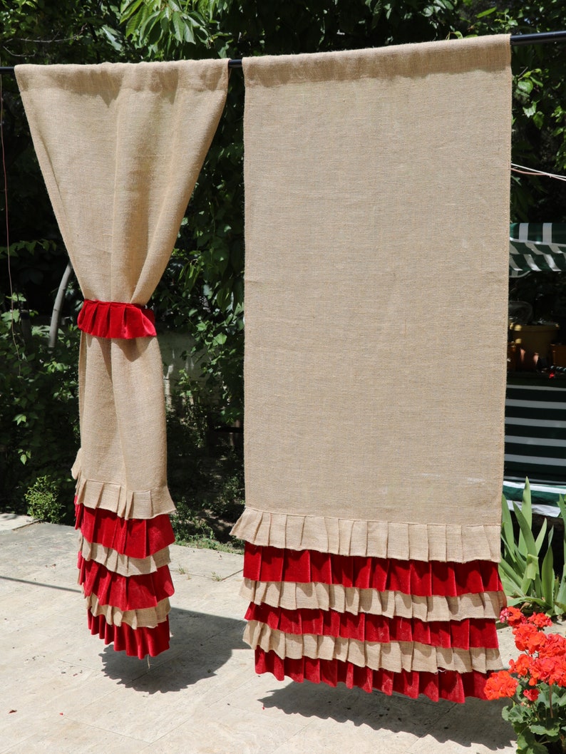 May include: Two burlap curtains with red velvet ruffles at the bottom. The curtains are hanging from a rod and are in a backyard setting.