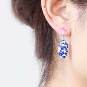 Può includere: Orecchini pendenti ovali con un motivo a mosaico di piastrelle in ceramica blu e bianca. Gli orecchini sono sospesi a ganci color argento. Un design classico ed elegante.