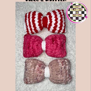 May include: Three handmade bow-shaped pillows in red and white, pink, and brown. The top pillow has red and white stripes. The text "BOW PILLOW TUTORIAL VIDEO & WRITTEN" is at the top. The pillows are on a white, textured surface.