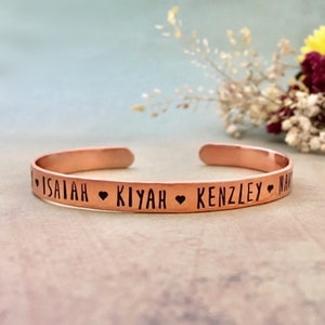 May include: A copper bracelet with the names Isaiah, Kiyah, and Kenzley engraved on it, separated by heart symbols.
