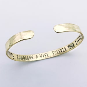 May include: A gold-colored cuff bracelet with a hammered texture. The bracelet has the engraved text: "TODAY A BRIDE, TOMORROW A WIFE, FOREVER YOUR LITTLE". The open cuff design allows for easy wear. Ideal for a wedding or anniversary gift.