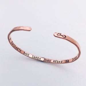 Thin stacking cuff bracelet in rose toned copper. Hand stamped inside is A fathers hug lasts long after he lets go with an infinity sign and heart design on the outside right end of the cuff. Simple, minimalist design to remember a lost loved one