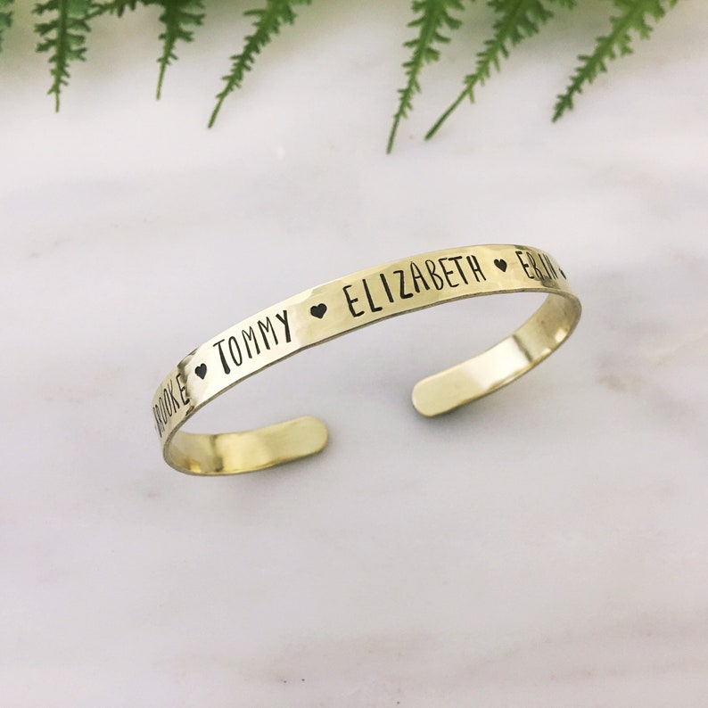 May include: Gold metal bracelet with the names Brooke, Tommy, Elizabeth, and Erin engraved on it, separated by heart symbols.