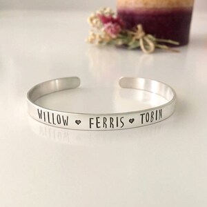 May include: Silver bangle bracelet with the names "Willow", "Ferris", and "Tobin" engraved on it, separated by heart symbols.