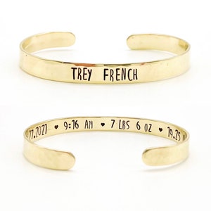 gold toned brass cuff bracelet with baby name on front and birth details on inside, separated by small black hearts. Name can be just first, first and middle, first and last, or full name.