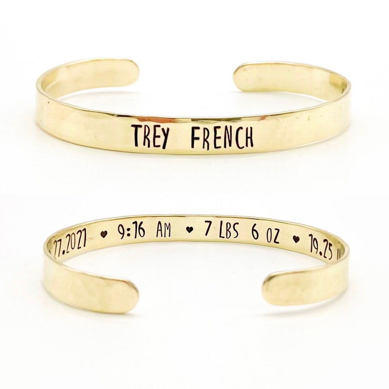 gold toned brass cuff bracelet with baby name on front and birth details on inside, separated by small black hearts. Name can be just first, first and middle, first and last, or full name.