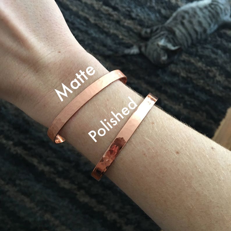 May include: Two copper cuff bracelets, one matte and one polished, are shown on a wrist. The matte bracelet is above the polished one. The word "Matte" is written above the top bracelet, and "Polished" is written above the bottom bracelet.