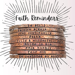 May include: A stack of copper-colored metal bracelets with inspirational quotes. The bracelets are stamped with phrases like "be still," "rejoice always," and "fear not." The words "Faith Reminders" are above the bracelets, with a sunburst design in the background.