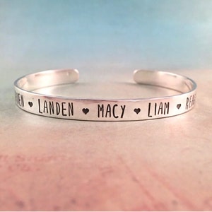 May include: Silver bangle bracelet with the names Landen, Macy, Liam, and Reese engraved on it, separated by heart symbols.