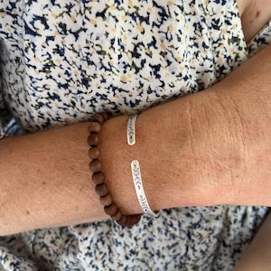 This skinny sterling silver cuff bracelet features a symmetrical leaf pattern across the front, with the text hidden inside. The bohemian style minimalist design makes this a great stacking bracelet to dress up or down. Here it is paired with a wooden beaded bracelet for an eclectic boho look.