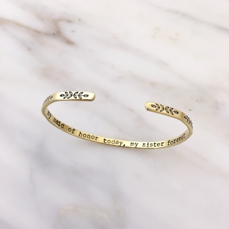 Golden brass skinny stacking cuff bracelet features a simple, hand stamped leaf design across the front with the saying my maid of honor today, my sister forever stamped inside. Text can be personalized. Outside finish can be matte or polished.
