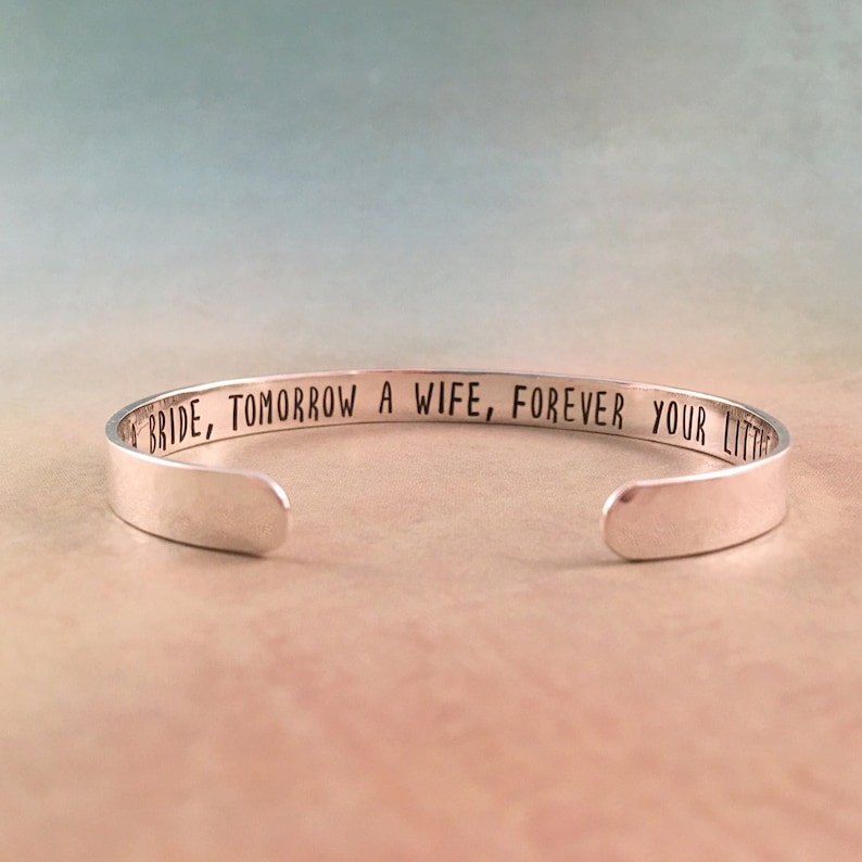 May include: A silver cuff bracelet with the engraved text: "Today a Bride, Tomorrow a Wife, Forever Your Little Girl." The bracelet has a simple, elegant design and is open at the bottom.
