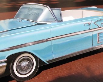 May include: A light blue convertible car model with a white interior. The car has a chrome bumper and trim, and the wheels are black with chrome hubcaps.