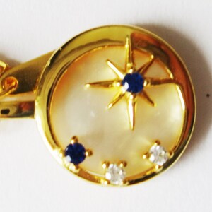 Peut inclure: Un collier en or avec un pendentif en forme de croissant de lune orné d'une étoile sertie de pierres bleues et de petites pierres blanches.