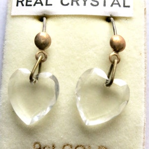 May include: A pair of heart-shaped crystal earrings with 9ct gold hooks. The earrings are on a white card with the words "REAL CRYSTAL" and "9ct GOLD" printed on it.