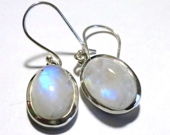 May include: A pair of silver-toned earrings featuring oval-shaped moonstone cabochons. The moonstones have a milky white base with iridescent blue and yellow flashes. The earrings have a simple hook design.