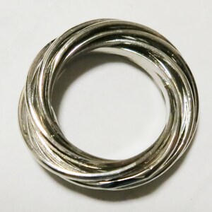 May include: A silver ring featuring an unusual design. The ring is made up of several interwoven bands, giving it a textured and complex look. The bands are smooth and reflective, reflecting light and creating highlights.