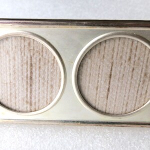 May include: A silver-toned double picture frame with two round openings. The frame has a textured surface and a simple design.