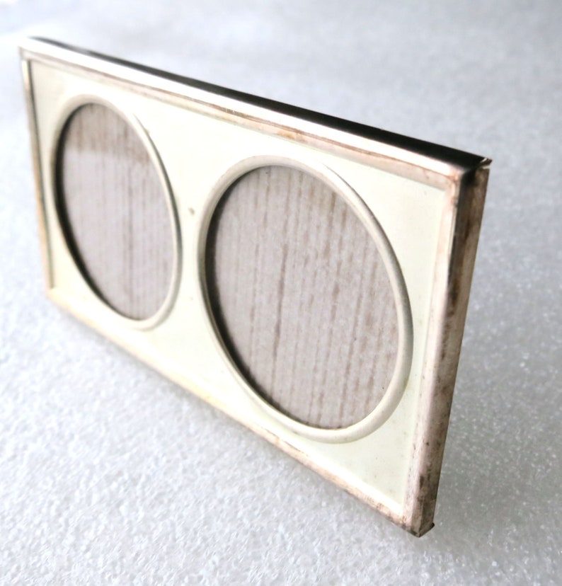 May include: A white double picture frame with a silver trim. The frame has two round openings for photos.