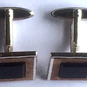 Puede incluir: Un par de gemelos de plata con piedras de ónix negro engastadas en un marco de madera marrón.