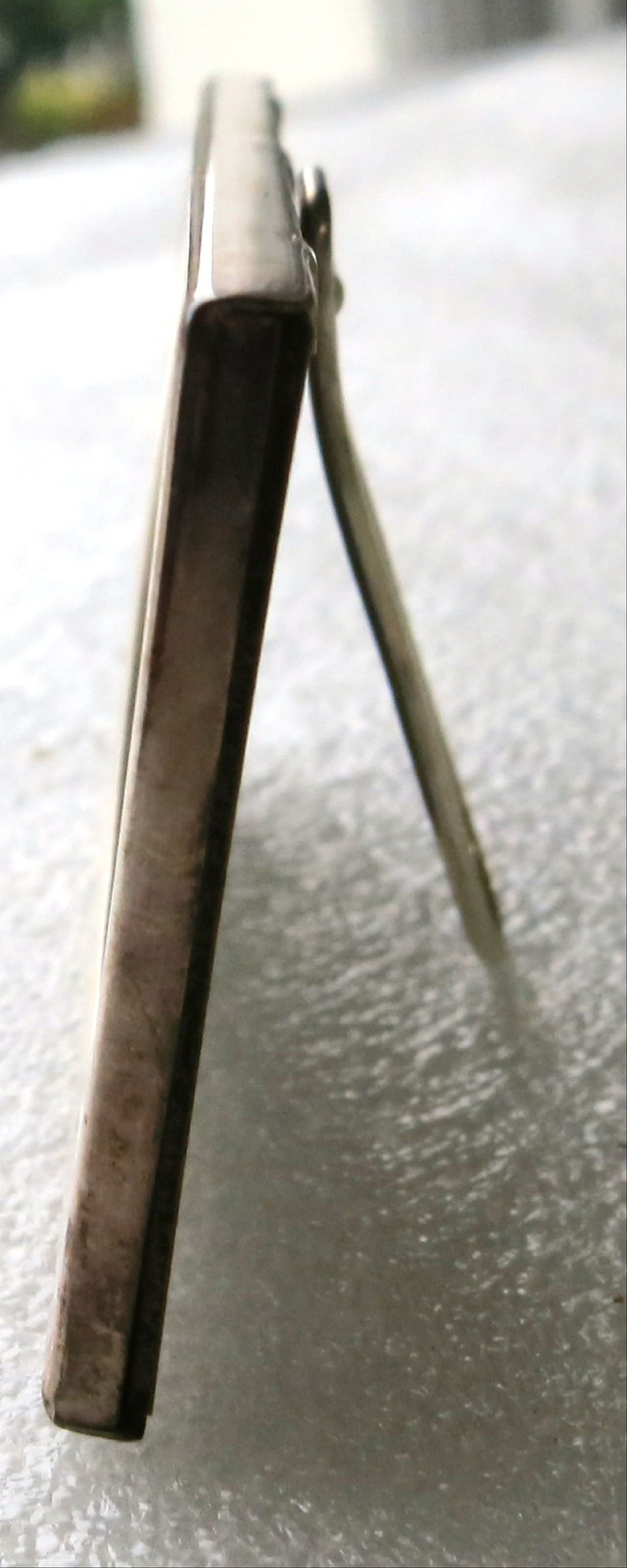 May include: Silver picture frame with a stand on the back. The frame is made of metal and has a polished finish.