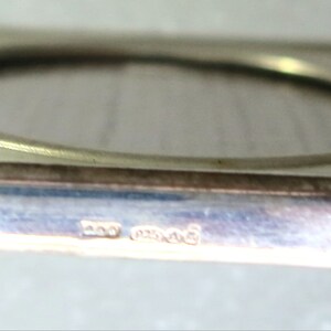 May include: A silver-toned square picture frame with a rounded opening. The frame has a hallmark on the bottom edge that reads "925 Mexico".
