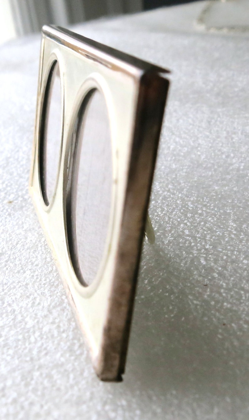 May include: A silver-toned double picture frame with two oval openings. The frame is made of metal and has a polished finish.