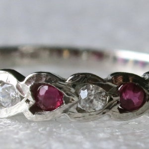以下が含まれることがあります： 繊細に絡み合ったデザインに、赤いルビーと透明なダイヤモンドが交互にセットされたシルバーのバンドリングです。