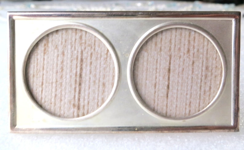 May include: A silver-toned double picture frame with two round openings. The frame has a smooth, polished finish and a simple, elegant design.