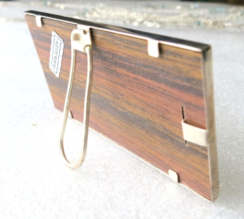 May include: A wooden picture frame with a silver metal frame and a silver metal stand. The frame has a label on the back that says "PLAT-O-LEY".