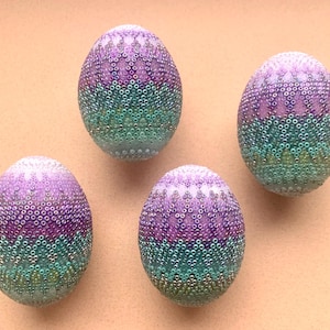 Könnte beinhalten: Vier dekorative Ostereier mit einem geometrischen Muster in Lila und Grün. Die Eier sind mit kleinen, schillernden Perlen bedeckt.
