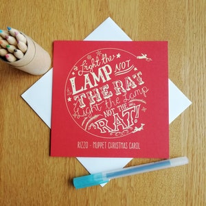 May include: Red card with white text that reads "Light the Lamp Not the Rat Light the Lamp Not the Rat" with the words "Rizzo - Muppet Christmas Carol" at the bottom.