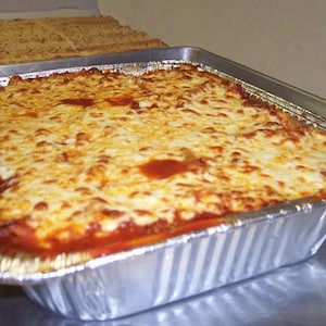 May include: A large rectangular tray of baked lasagna, topped with melted cheese. The lasagna is in a disposable foil tray. Slices of garlic bread are visible in a box in the background.