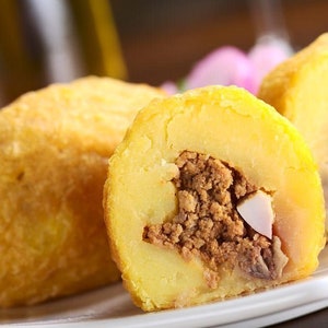 Peut inclure: Gros plan sur une assiette avec trois boules de pommes de terre farcies, de couleur jaune doré. La garniture est un mélange de viande hachée et d'un morceau de viande blanche. Plat traditionnel.