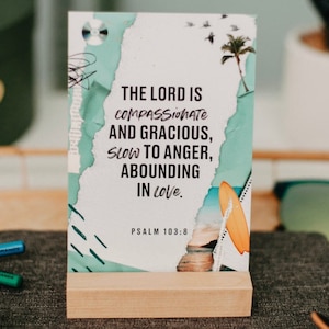 May include: A wooden stand with a white card featuring a colorful design and the text "THE LORD IS COMPASSIONATE AND GRACIOUS, SLOW TO ANGER, ABOUNDING IN LOVE. PSALM 103:8"