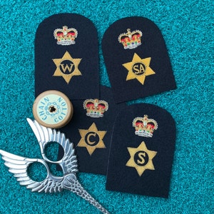 May include: Four black fabric patches with gold embroidery. Each patch features a crown, a star, and a letter. The letters are W, SA, C, and S.