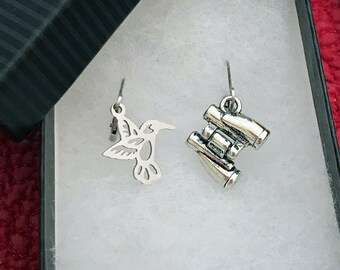 May include: A pair of silver earrings, one shaped like a hummingbird and the other like a pair of binoculars.