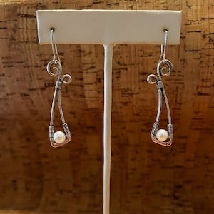 May include: Silver wire earrings with a pearl dangling from the bottom of each earring.