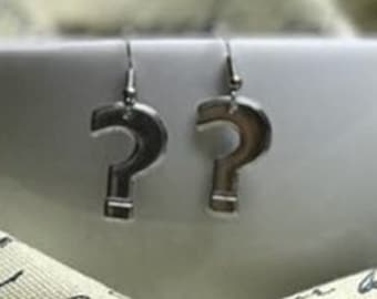 May include: A pair of silver question mark earrings. The earrings are hanging from a white surface.